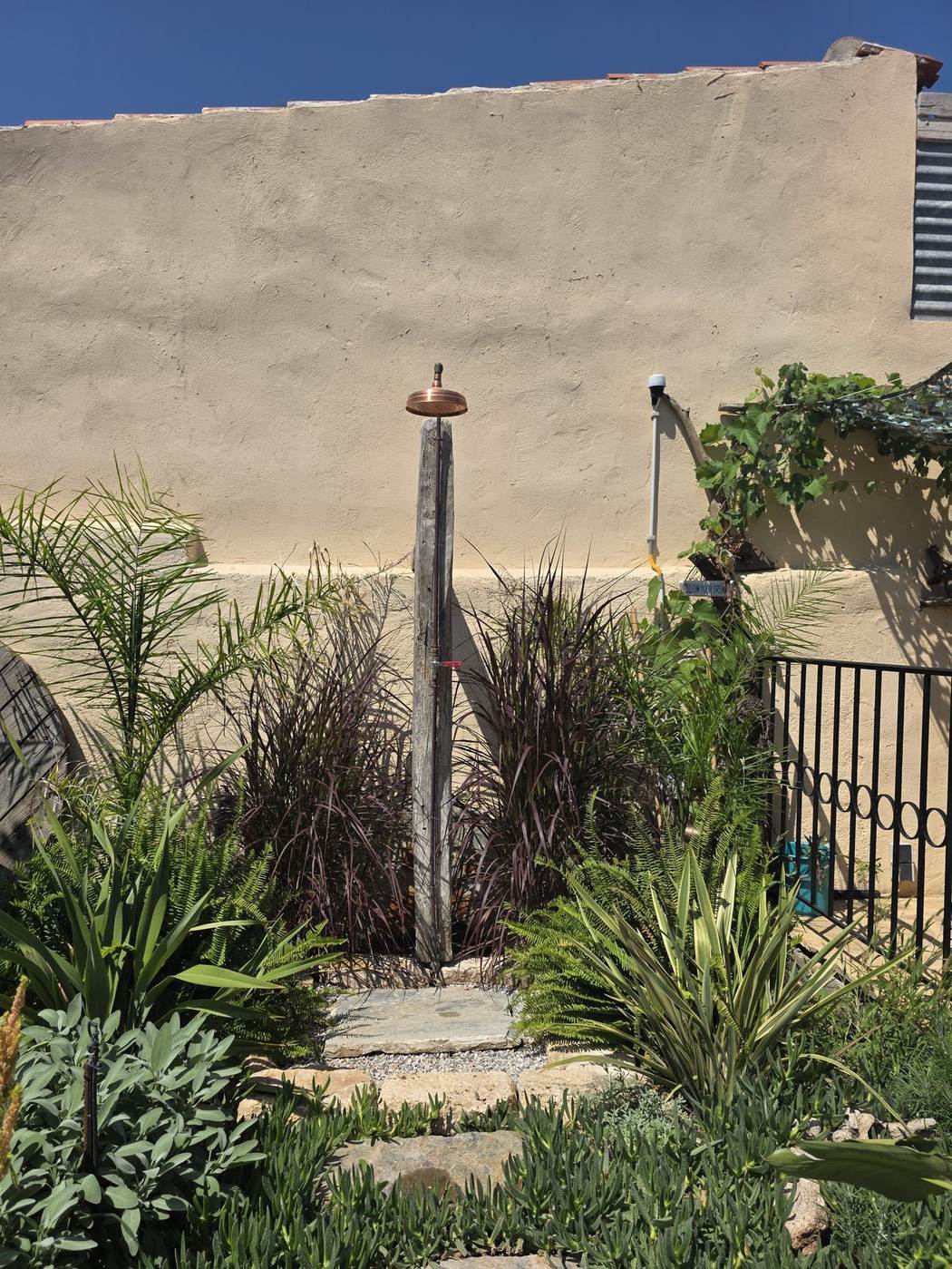 Copper outdoor shower on a weathered beam among the ornamental grasses
