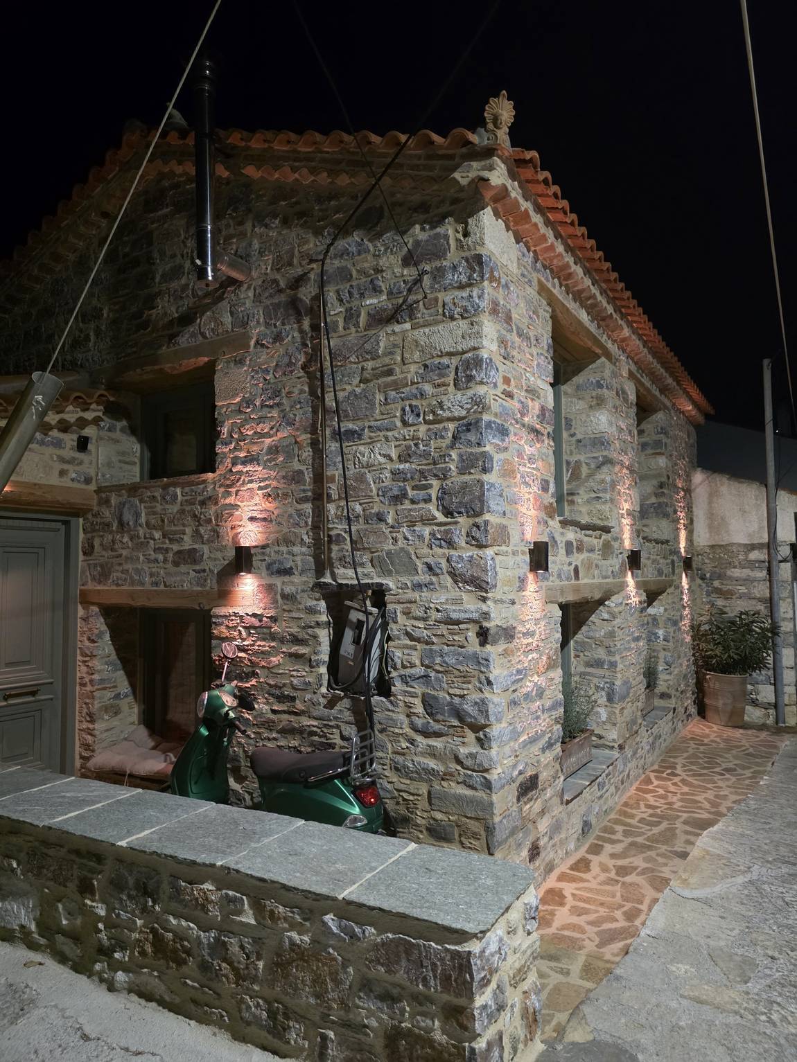 The lit stone facade with a green Vespa in front of it